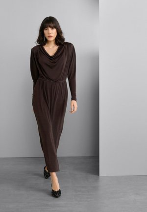 Robe longue en jersey brun foncé avec un col bénitier drapé, des manches longues, une taille cintrée et une silhouette à jambes droites. Talons noirs cloutés.