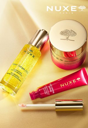 Quatre produits de soin NUXE sur un fond doré : un sérum jaune dans un flacon transparent, un pot de crème rose et un tube rouge avec embout applicateur.
