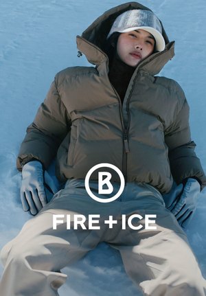 Kurtka puchowa w oliwkowej zieleni, z wysokim kołnierzem i pełnym zamkiem błyskawicznym, zestawiona z jasnobeżowymi spodniami i szarymi rękawiczkami, na tle zaśnieżonego krajobrazu.