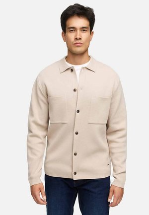 Beige Hemdjacke aus weichem Material, mit zwei Vorderentaschen, einem Hemdkragen und braunen Knöpfen. Trägt man über einem weißen T-Shirt.