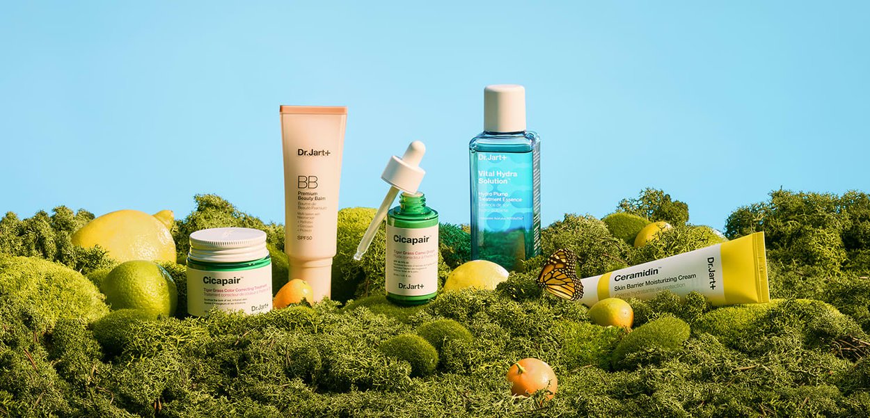 Dr.Jart+ huidverzorgingsproducten op groen mos met citroenen, limoen en een vlinder onder een helderblauwe hemel.