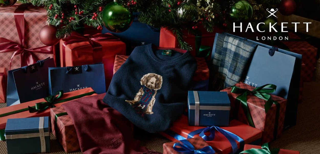 Suéter azul marino con un diseño bordado de un perro, rodeado de regalos envueltos y bolsas de regalo en varios colores y patrones.