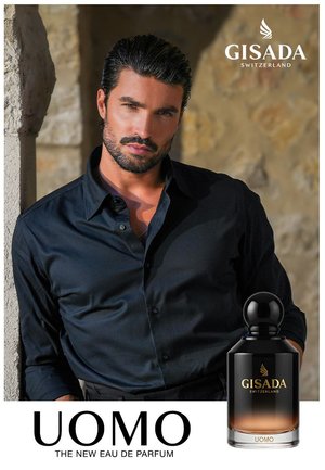 Mann mit dunklem Haar und Bart, der ein schwarzes Hemd trägt und sich an einer Steinmauer neben einer schwarzen und bernsteinfarbenen Gisada UOMO Parfümflasche anlehnt.