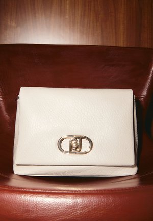 Borsa a mano bianca in pelle con finitura testurizzata, dotata di una chiusura dorata e un design semplice e rettangolare. Appoggiata su una superficie marrone.