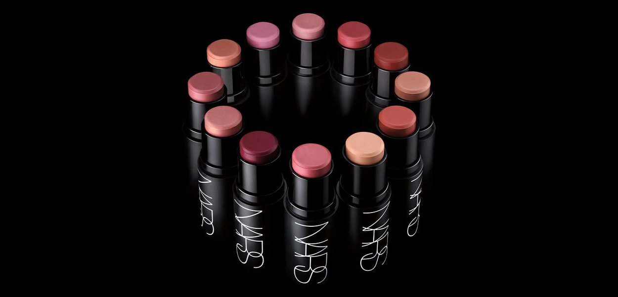 Circle of twelve lipsticks with black cylindrical tubes. Shades include pink, mauve, and coral. Smooth texture with rounded tops.