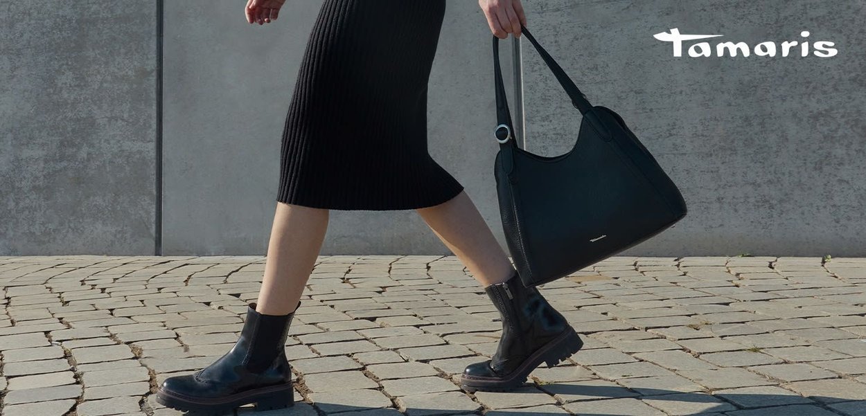 Black leather handbag with a smooth texture and adjustable strap, paired with a ribbed black dress and chunky black ankle boots.