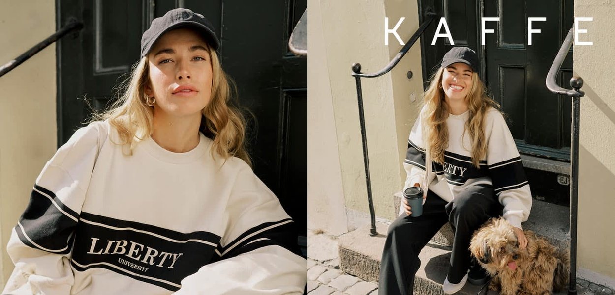 Junge Frau mit schwarzer Mütze und Liberty-Sweatshirt sitzt auf den Stufen vor einem Café, hält eine Kaffeetasse und streichelt einen kleinen Hund.