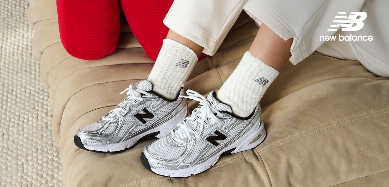 Silver athletic shoes with black accents, mesh material, and a thick white sole, paired with cream ribbed socks, displayed on a neutral surface.