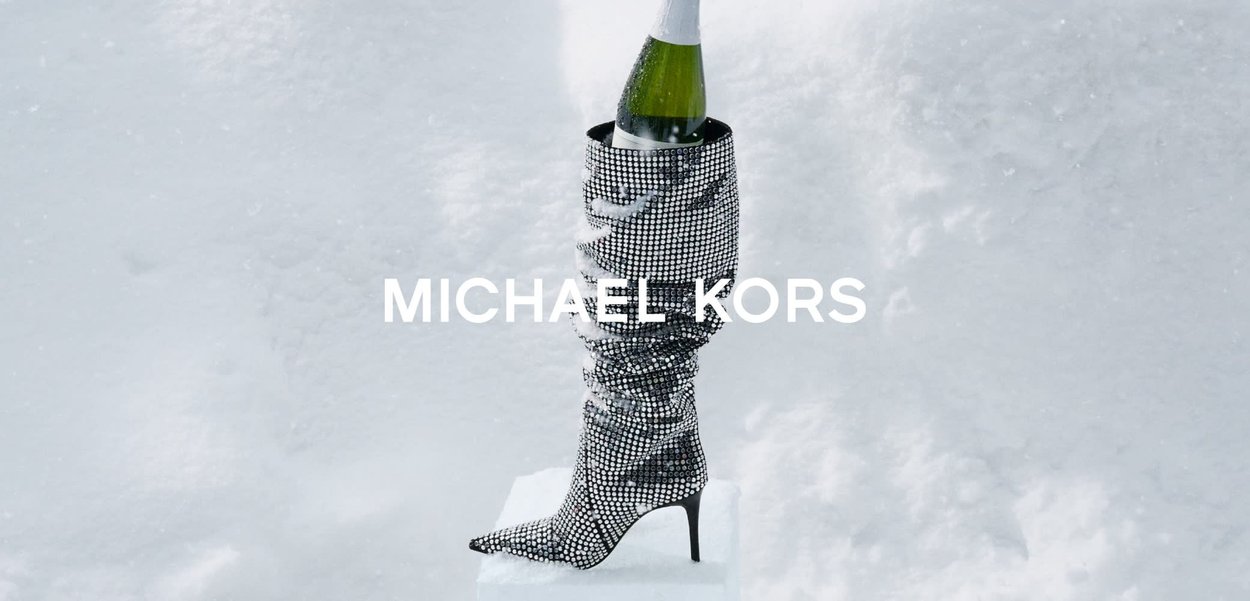 Bota de tacón alto hasta la rodilla en plata metálico, adornada con piedras de strass y una textura fruncida. Sostiene una botella de champán en la abertura.