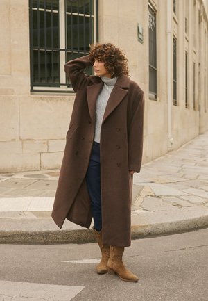 Ruskea villakangastakki kaksirivisellä napituksella, leveillä kaula-aukoilla, yhdistettynä vaaleanharmaaseen pooloneuleeseen, sinisiin farkkuihin ja beigeihin nilkkureihin.