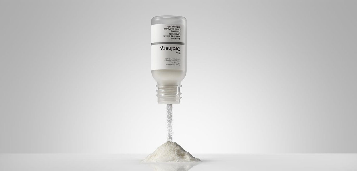 White powder product in a transparent bottle, cap off, with powder spilling into a small mound. Label features black text on a white background.