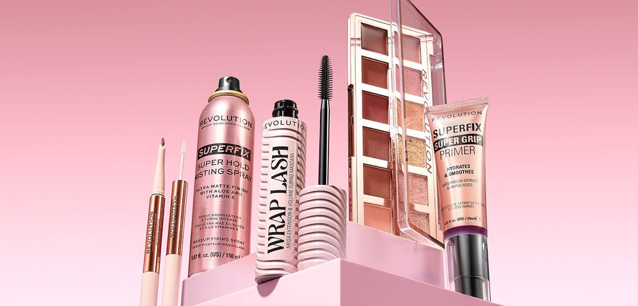 En samling sminkeprodukter som inkluderer en rosa sprayboks, en maskarabørste og en palett med nøytrale nyanser, med varierende glansfinish.