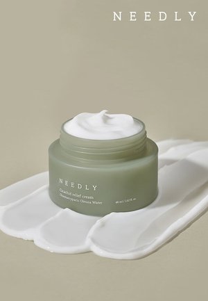 Barattolo di vetro verde di crema cicatrizzante per il sollievo, con una texture di crema bianca in cima, circondato da una macchia di crema bianca su una superficie beige.