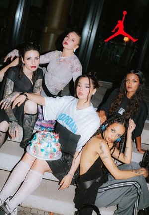 Group of five individuals seated on steps, showcasing diverse styles: oversized Jordan shirt, tattoos, lace stockings, and a decorated cake.