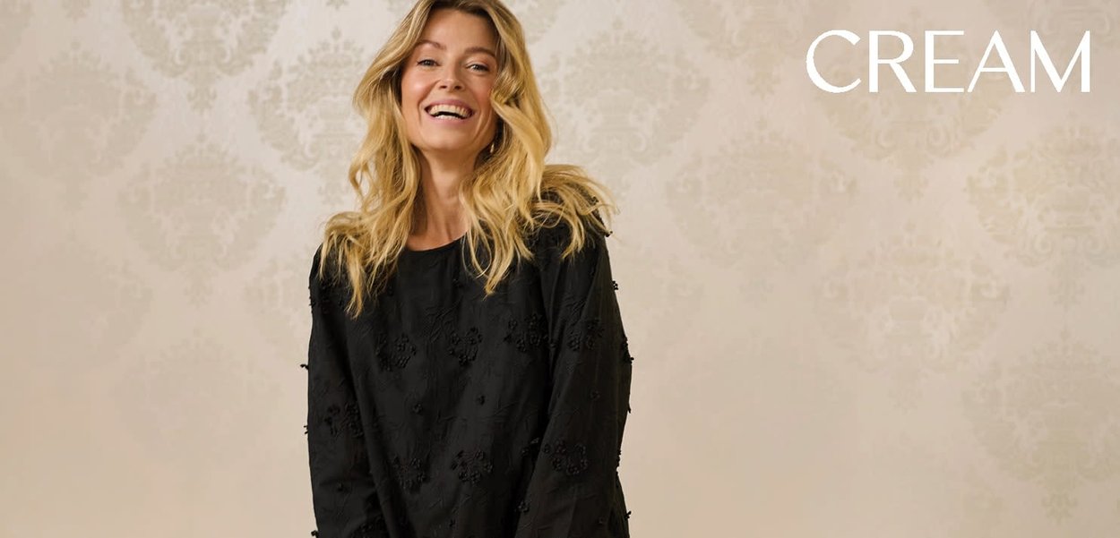 Schwarzes langärmliges Oberteil mit strukturierten Blumenverzierungen, Rundhalsausschnitt, lockerem Schnitt und leichtem Stoff. Der Hintergrund zeigt ein dezentes Muster.