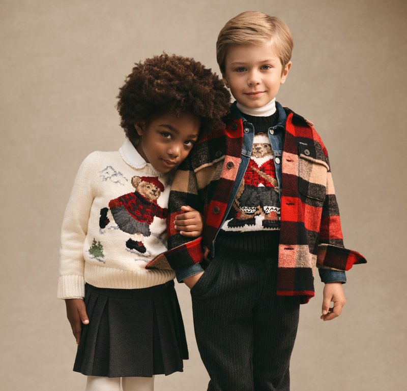 Knitted cream sweater with bear design, grey pleated skirt; boy in plaid jacket and sweater with embroidered figure, dark trousers.