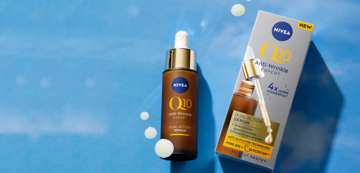 Bottiglia e scatola del siero Nivea Q10 Anti-Wrinkle Expert Dual Action su sfondo blu, con gocce di siero attorno alla bottiglia.
