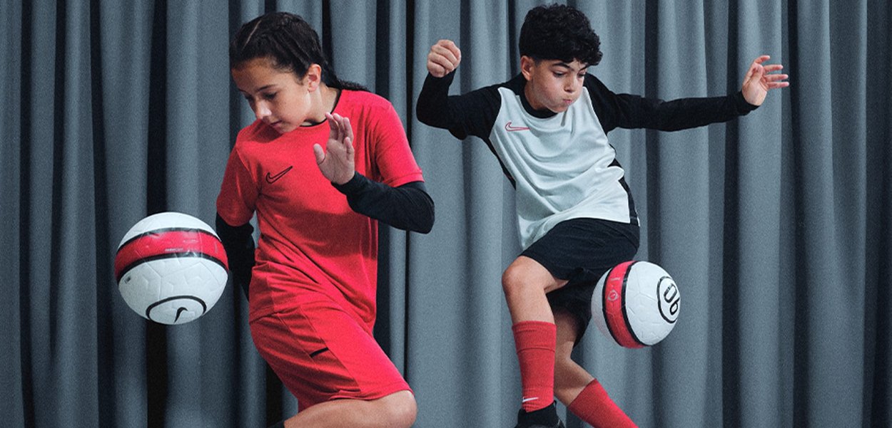 Due bambini in abbigliamento sportivo mostrano le loro abilità nel calcio. Uno indossa una maglietta e pantaloni corti rossi, l'altro una maglietta bianca e nera con pantaloni corti neri.