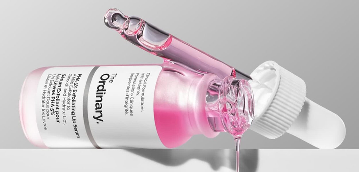 Pink liquid lip serum in a clear glass bottle with a white dropper cap, featuring a smooth finish and visible liquid texture.