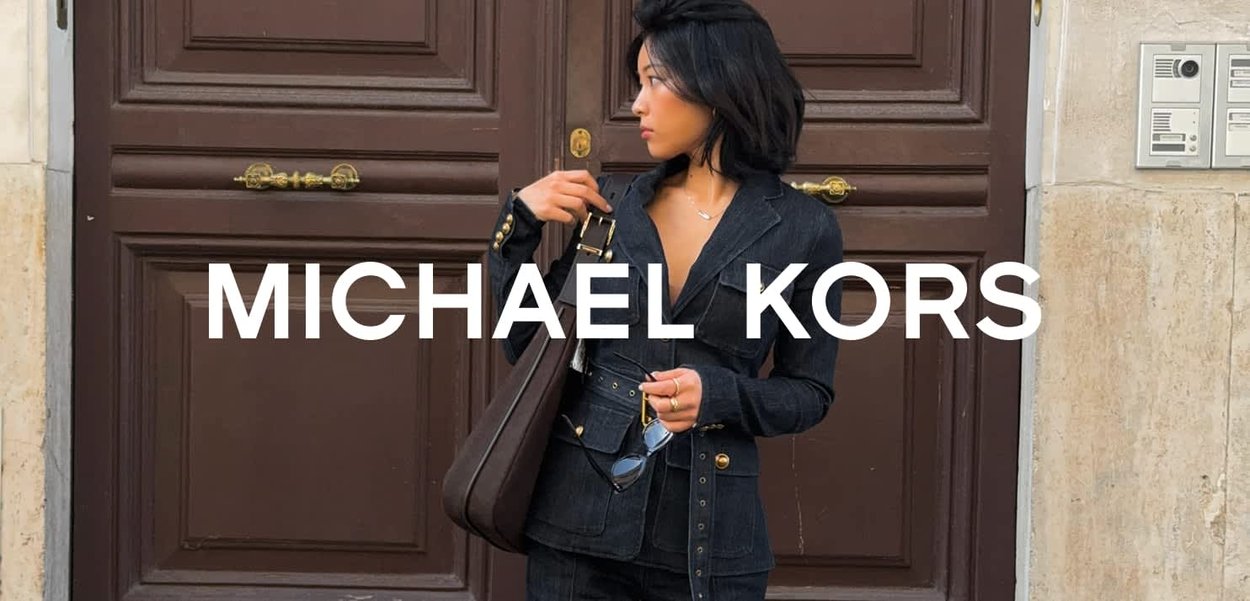 Blazer de denim con detalles en dorado, combinado con jeans oscuros. Un bolso marrón y gafas de sol complementan el atuendo frente a un fondo de puerta de madera.