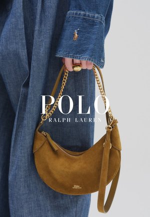 Ręka trzymająca brązową torebkę w kształcie półksiężyca zamszową na złotym łańcuszku, ubraną w niebieski denimowy strój z haftowanym logo Polo na rękawie.