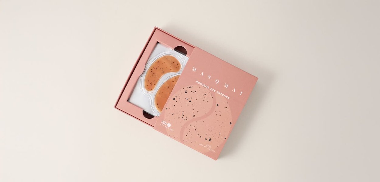 Boîte de couleur pêche contenant deux patches pour les yeux en gel. Les patches ont la forme de croissants de lune avec un motif tacheté. Le texte affiche le nom du produit et les détails.