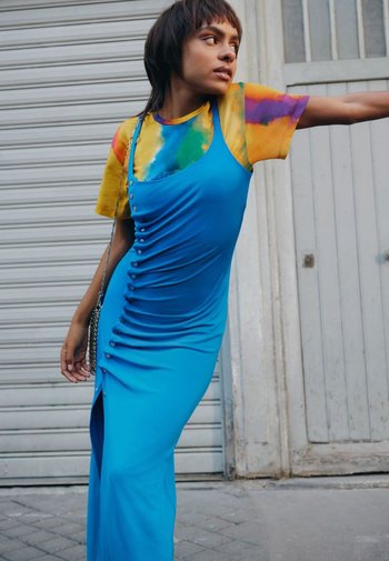 Niebieska sukienka bodycon z guzikami, zestawiona z koszulą z krótkim rękawem w technikę tie-dye, o żywych kolorach. Gładki materiał, dopasowany krój.