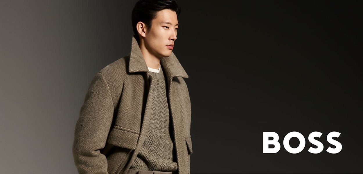 Manteau en laine beige avec un col surdimensionné et un motif texturé. Porté sur un pull léger, le modèle pose devant un fond sombre. Marque BOSS visible.