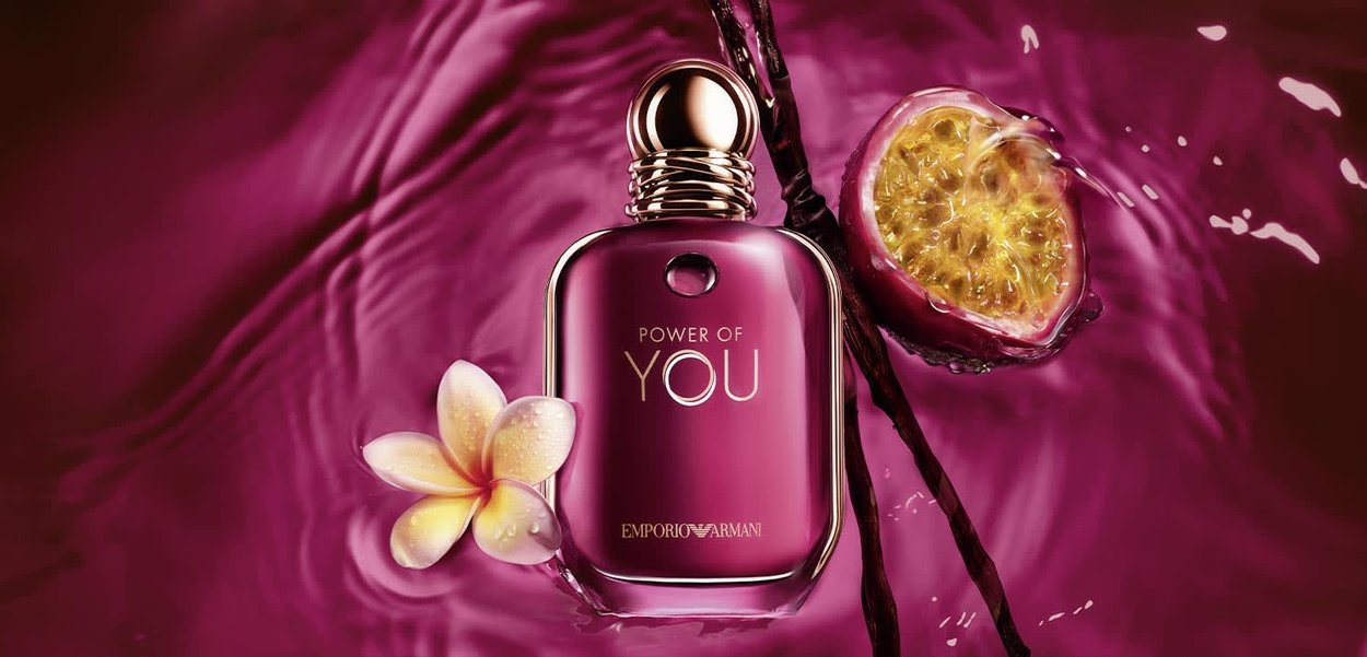 Bottiglia di profumo viola con etichetta "Power of You", accompagnata da un fiore di plumeria, bacche di vaniglia e frutto della passione tagliato a metà che galleggiano su un liquido viola corrispondente.