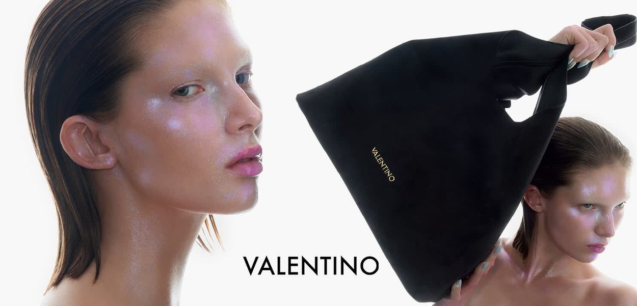 Zbliżenie na modelkę z mokrą skórą trzymającą czarną torbę typu tote Valentino z złotym logo na białym tle.