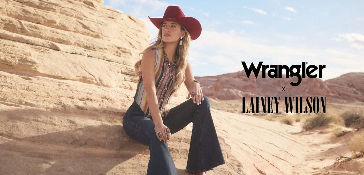 Brown and white striped sleeveless top with buttons, blue bell-bottom jeans, and a red wide-brimmed hat against a rocky landscape.