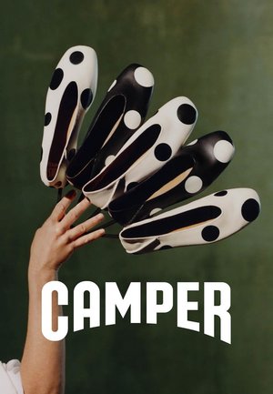 Ręka trzymająca sześć czarno-białych wsuwanych butów w kropki, rozłożonych wachlarzowo na zielonym tle, z napisem „CAMPER” poniżej.