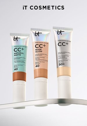 Drei Tuben IT Cosmetics CC+ Cream in den Farbtönen Natural Matte, Nude Glow und SPF 50+ Hydrating Serum auf einer gewölbten Oberfläche.
