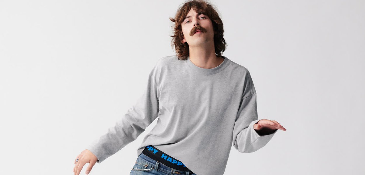 Graues Langarmshirt mit lockerer Passform, kombiniert mit Jeans mit blau akzentuiertem Bund. Glatte Textur vor einem schlichten weißen Hintergrund.