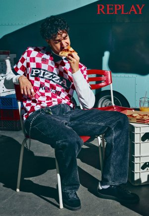Rød og hvit rutet skjorte med korte ermer og teksten "PIZZA", paret med mørke denim bukser. Individuell sitter på en stol og holder en pizzabit.