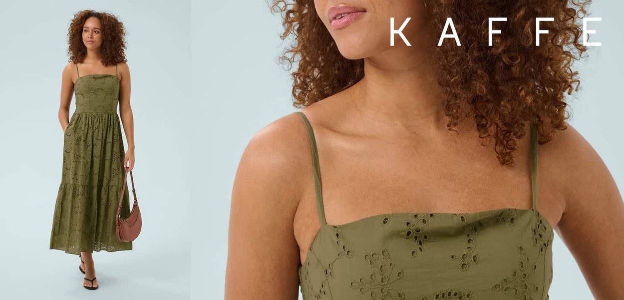 Woman with curly hair wearing a green eyelet midi dress with thin straps, carrying a small brown bag and wearing black sandals, on light background.