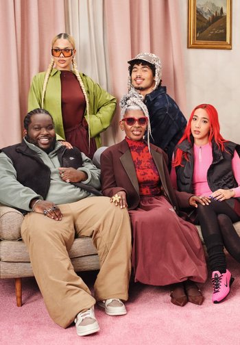 Gruppo di cinque persone sedute su un divano beige davanti a un tappeto rosa. Stili e colori di abbigliamento vari, tra cui verde, bordeaux, rosa e accessori con motivi.