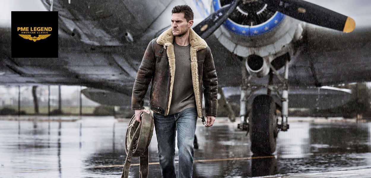 Bruin shearling-voering leren jack, grijze trui, blauwe jeans en een tas, voor een militaire straaljager in regenachtige omstandigheden.