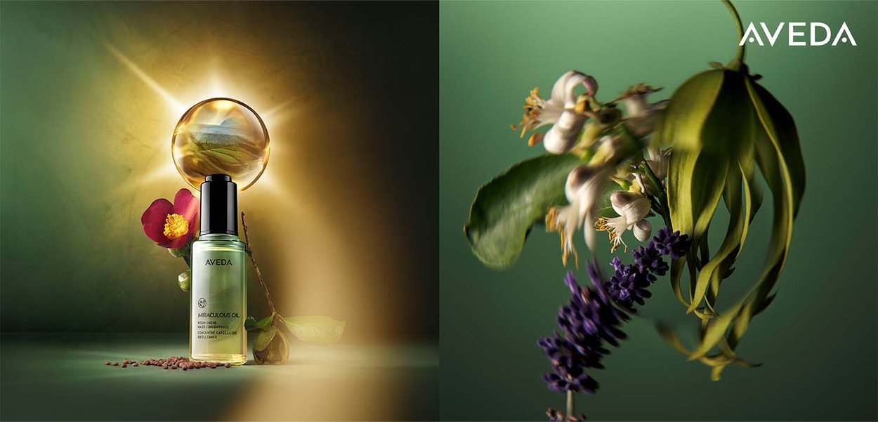 Bottiglia di vetro trasparente di Aveda Miraculous Oil davanti a un orb luminoso, circondata da fiori colorati e fogliame verde su uno sfondo tenue.