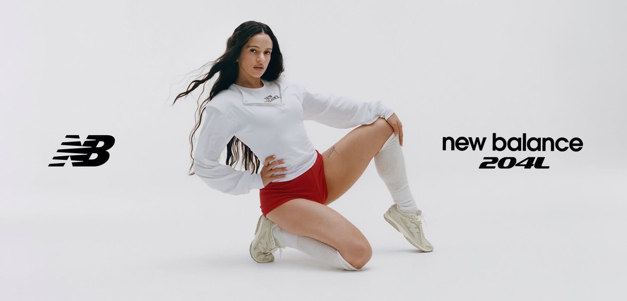 Mujer con camisa blanca de manga larga, pantalones cortos rojos, calcetas hasta la rodilla y zapatillas New Balance 204L posando de rodillas frente a un fondo blanco con logotipos de la marca arriba y abajo.