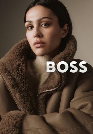 Chaqueta marrón de gran tamaño con un suave cuello de borreguito y una textura de cuero lisa. Capa sobre un cuello de tortuga color beige claro. Texto en negrita "BOSS".