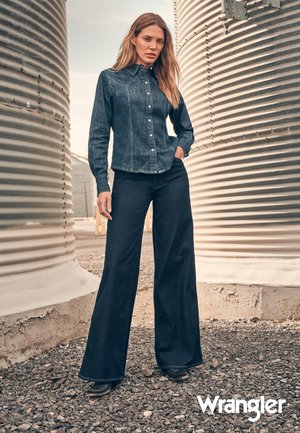 Jeansskjorte med knapper og spiss krage, sammen med høyt liv og utsvingte jeans. Fargen er mørk blå, med glatt tekstur og enkelt design.