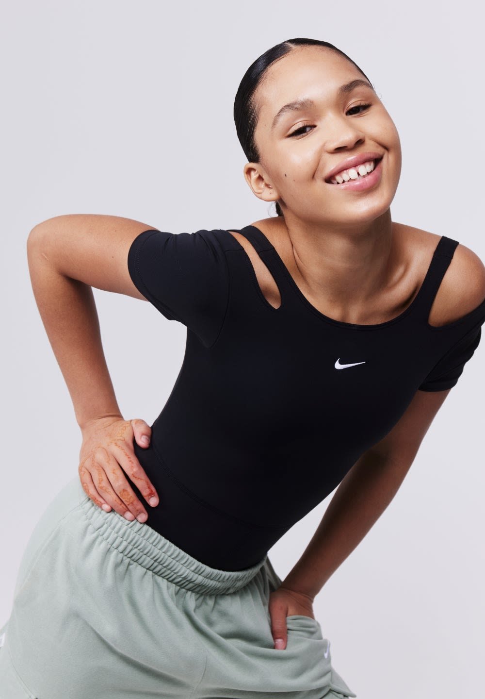 Black athletic bodysuit with cut-out shoulder design, featuring a small white logo. Paired with light green elastic waistband shorts.