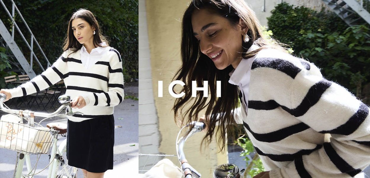 Pullover a righe bianche e nere con colletto, indossato sopra una gonna nera. Modella sorridente mentre tiene il manubrio di una bicicletta.