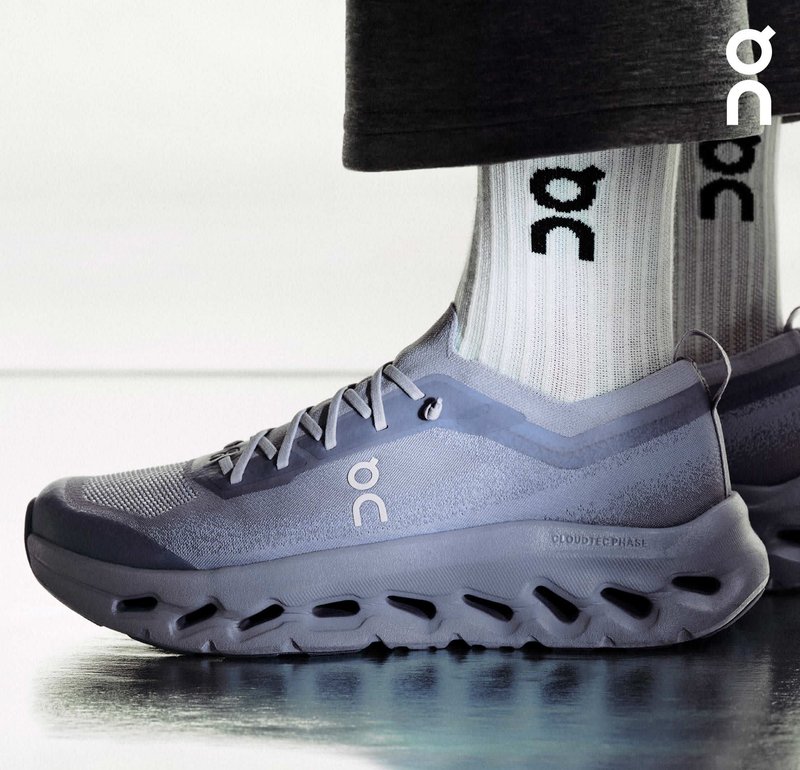 Leichter grauer Sportschuh mit einem Obermaterial aus Mesh, texturiertem Design und Schaumsohle mit Aussparungen. Kombiniert mit weißen gerippten Socken.