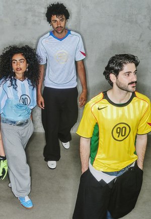 Tre persone indossano magliette sportive: una azzurra chiara con un motivo a scacchi, una a strisce gialle e verdi e un'altra in tonalità blu.