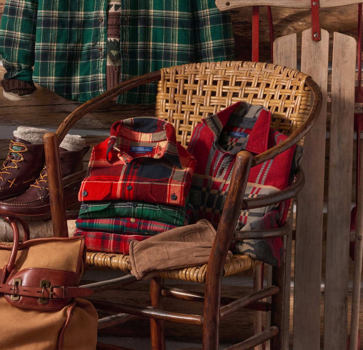 Punaisen, vihreän ja mustan ruudullisen flanellipaidat pinottuna punotulle tuolille. Lähellä ruskeat nahkahansikkaat ja tukevat ruskeat saappaat harmaalla vuorella.