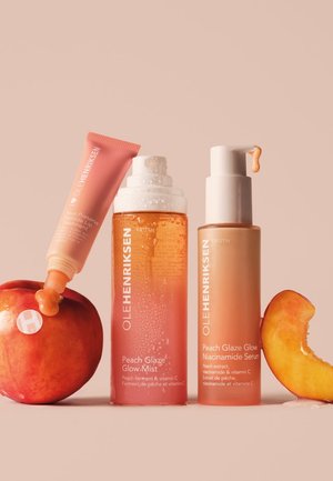 Peach Glaze products in pink and orange bottles, featuring a serum, mist, and lip treatment, alongside a fresh peach and slice.