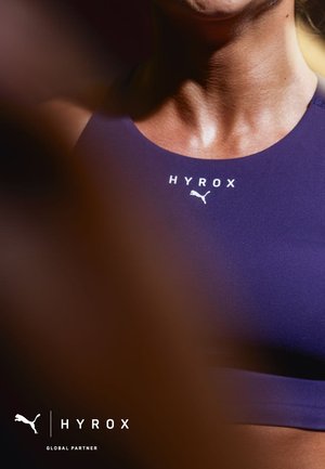 Primer plano de una persona que lleva una camiseta deportiva morada con los logotipos de "HYROX" y Puma visibles en la zona del pecho.