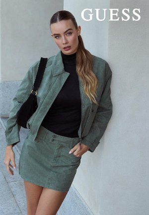 Chaqueta vaquera verde con cremallera frontal, combinada con un suéter de cuello alto negro y una falda vaquera verde a juego. Tejido texturizado y diseño estructurado.